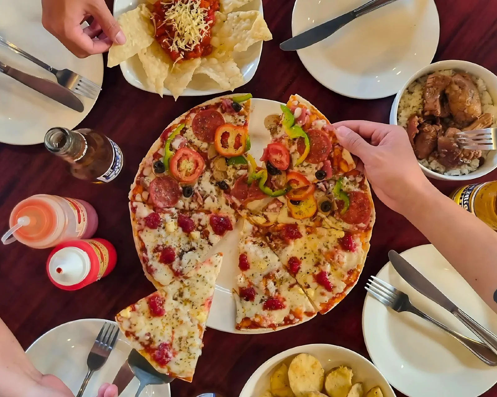 Friends sharing a Handuraw thin-crust pizza, nachos and rice meals around a table